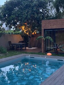 La terrasse éclairée sous le néflier le soir, avec la piscine au premier plan